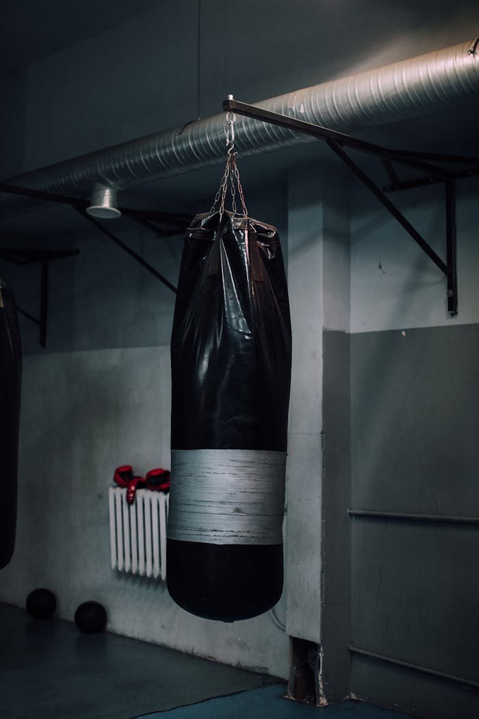A hanging black punching bag in a dimly lit gym, highlighting sports equipment.
